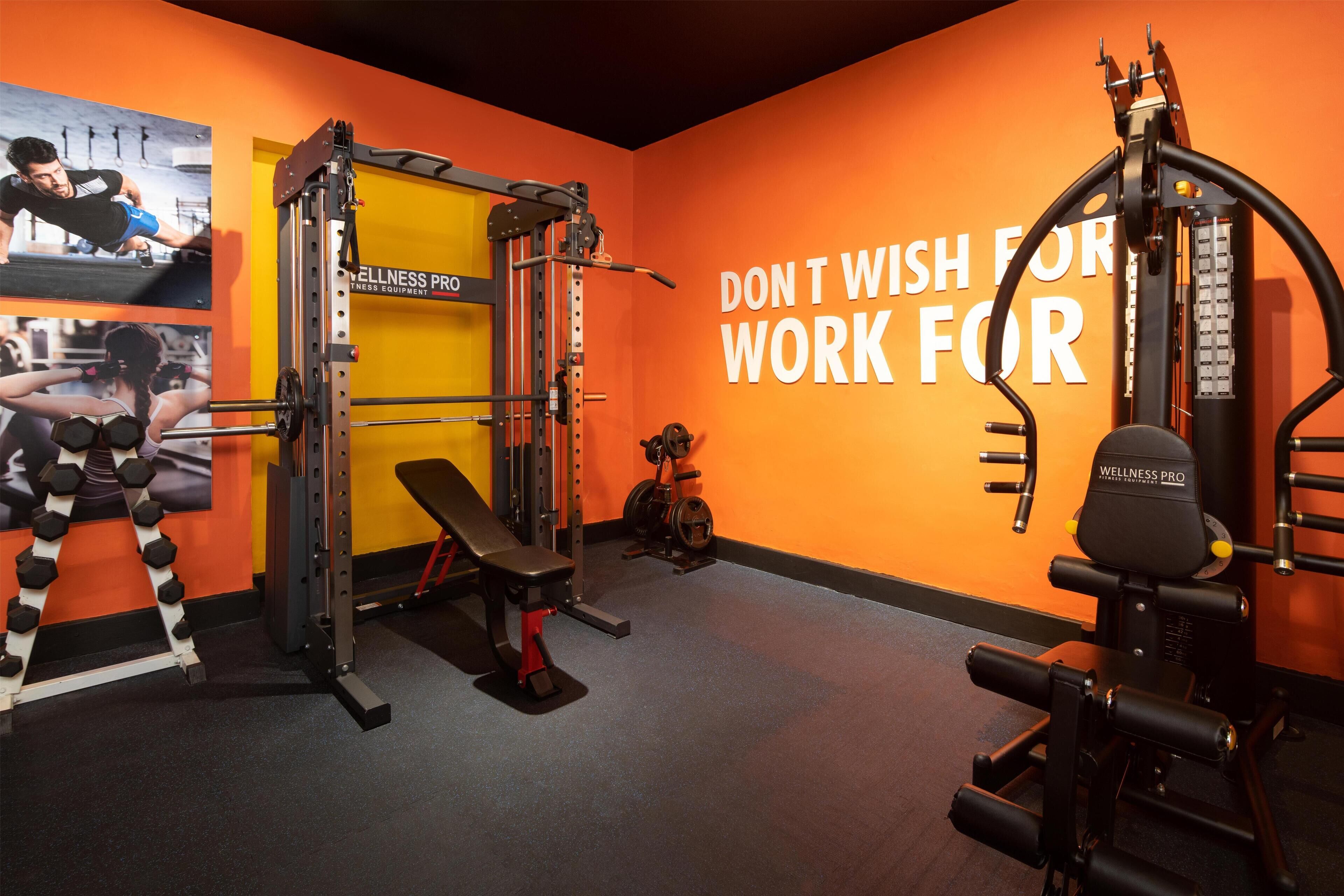 Un gimnasio con varios equipos de ejercicio, una banca y un letrero motivacional en la pared.