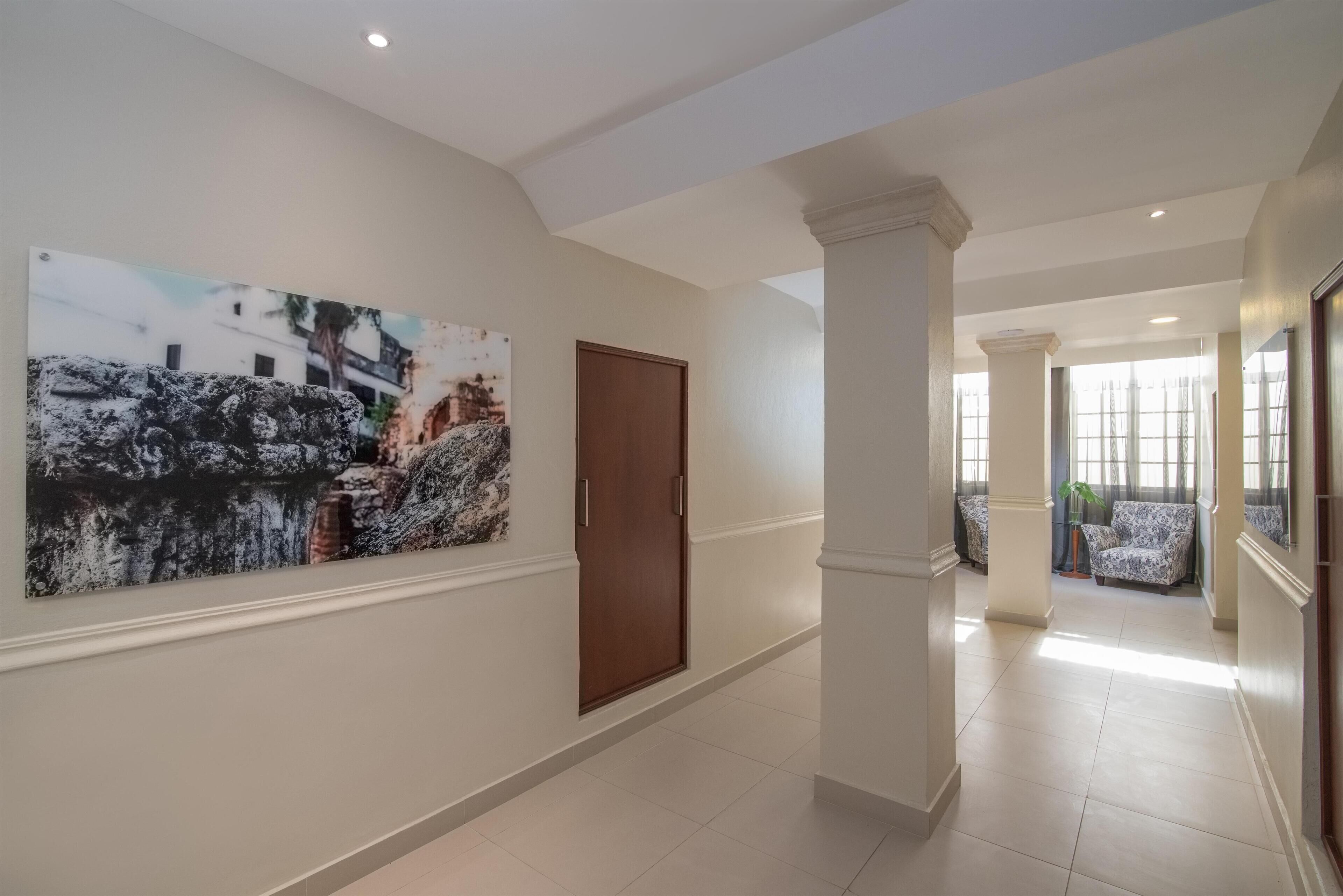 Un couloir avec une porte en bois, un grand tableau abstrait et un coin salon avec des fauteuils à motifs.
