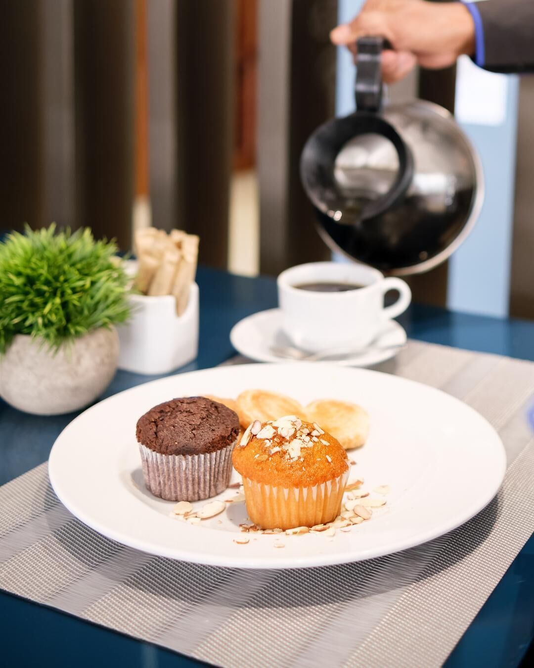 A breakfast setting with a plate of muffins, a cup of coffee, and a teapot.