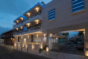 Un hotel de varios pisos con balcones, una entrada cubierta y un área de estacionamiento.