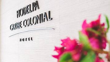 En skylt för ”Hotel Modelo Caribe Colonial” med en del av utsikten över rosa blommor.
