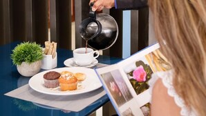 A person pouring coffee into a cup on a table with a muffin and a small plant.