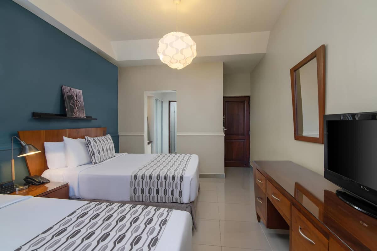 Ein Hotelzimmer mit zwei Betten, einem Fernseher, einem Schreibtisch und einem Spiegel.