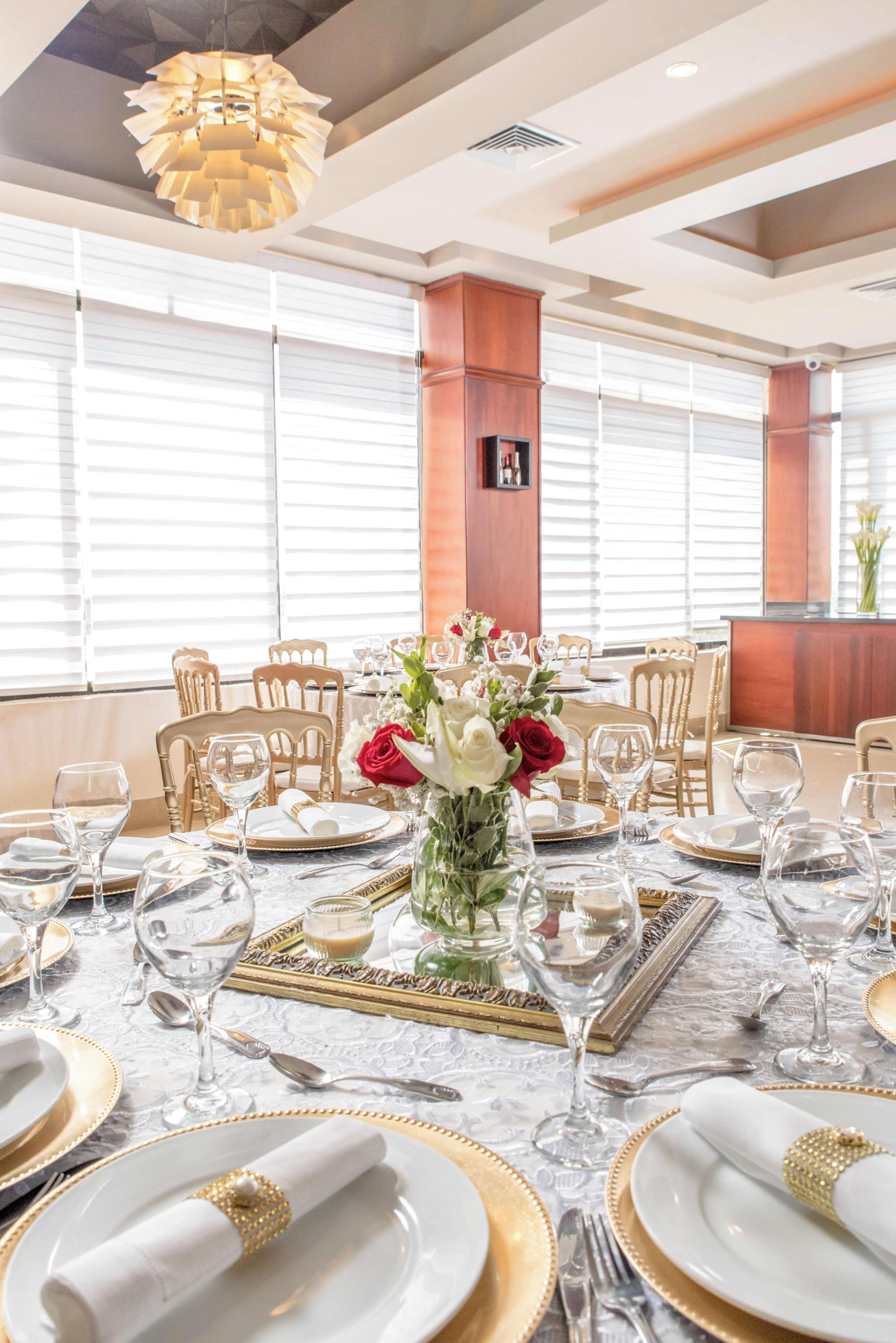 A dining area with a table set for a meal, chairs, a chandelier, and large windows with blinds.