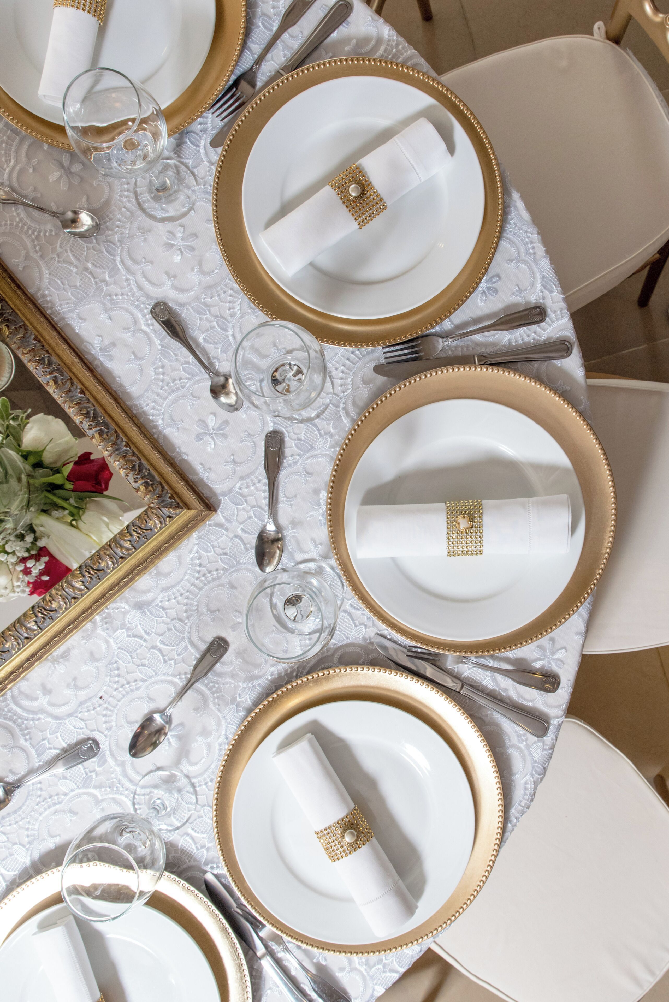 Una mesa dispuesta con platos blancos, detalles dorados y cubiertos.