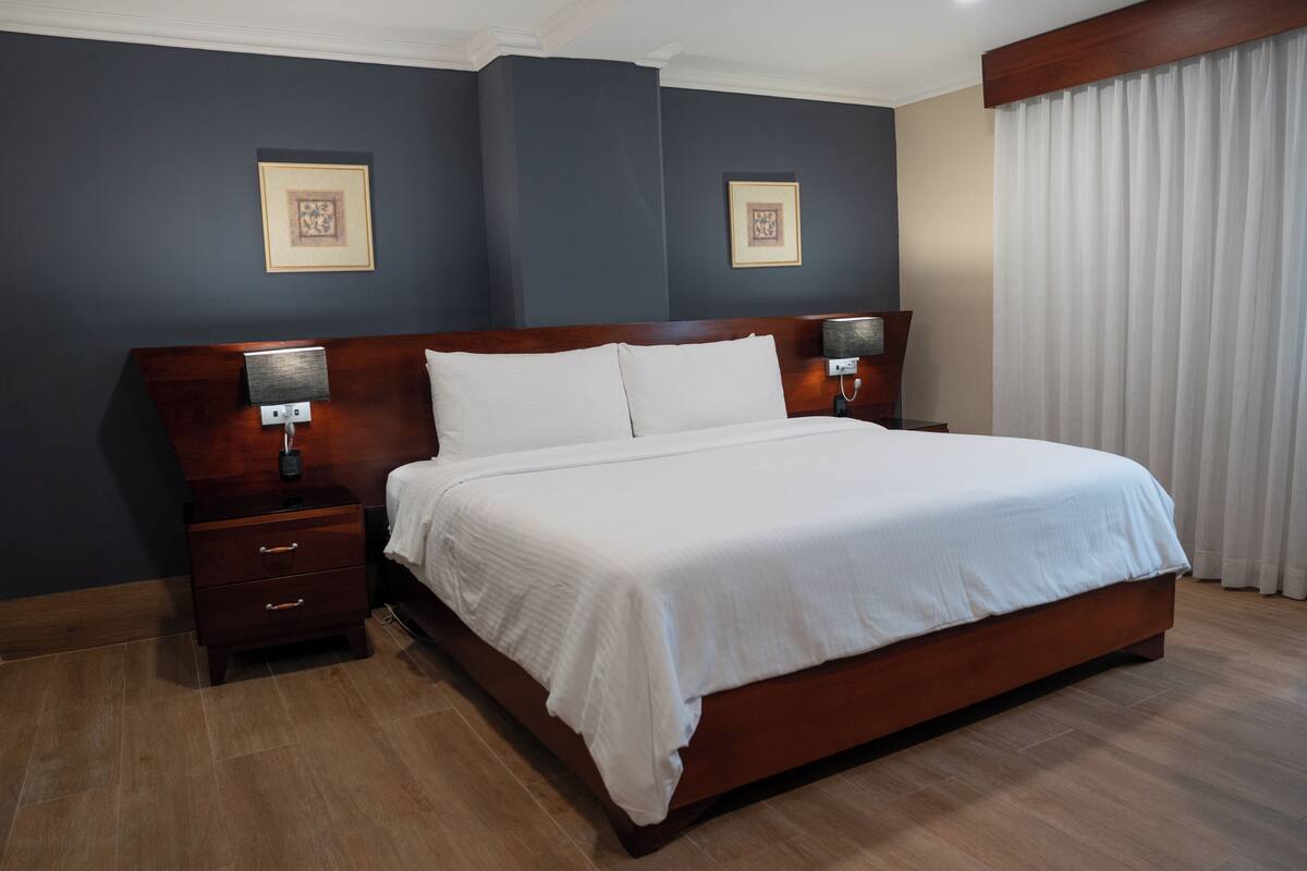 A hotel room with a large bed, wooden headboard, bedside tables, wall-mounted lamps, and framed artwork.