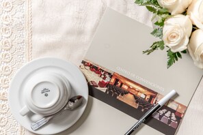 Enjoy a refined table setting with a white cup, saucer, and silver spoon, accompanied by a brochure and a pen.