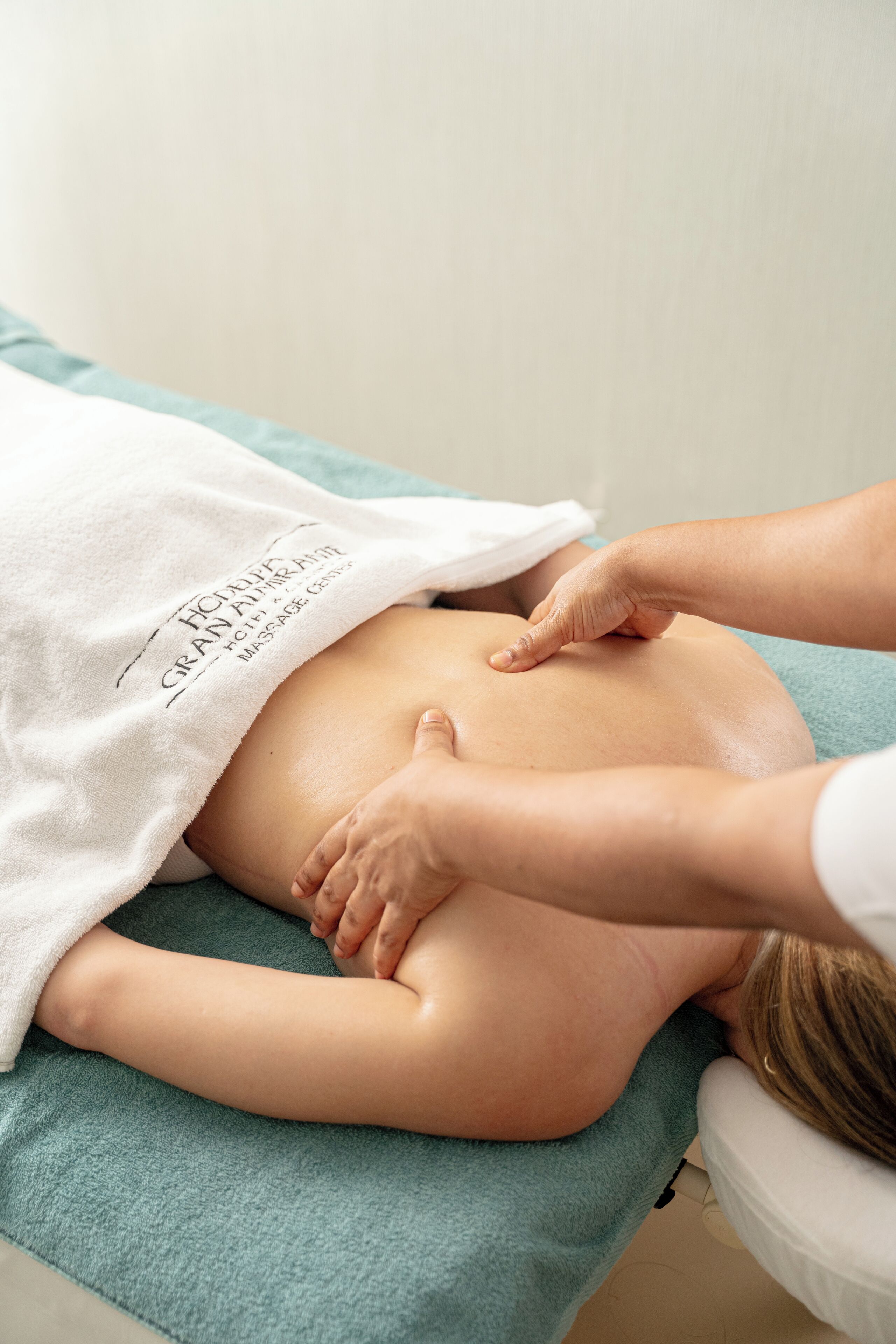 A massage therapy session in progress, with a towel covering the client and a massage therapist's hands on the client's back.