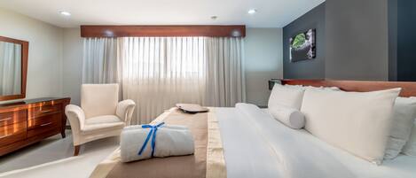 A hotel room with a bed, a chair, a dresser, a scale, and a painting on the wall.