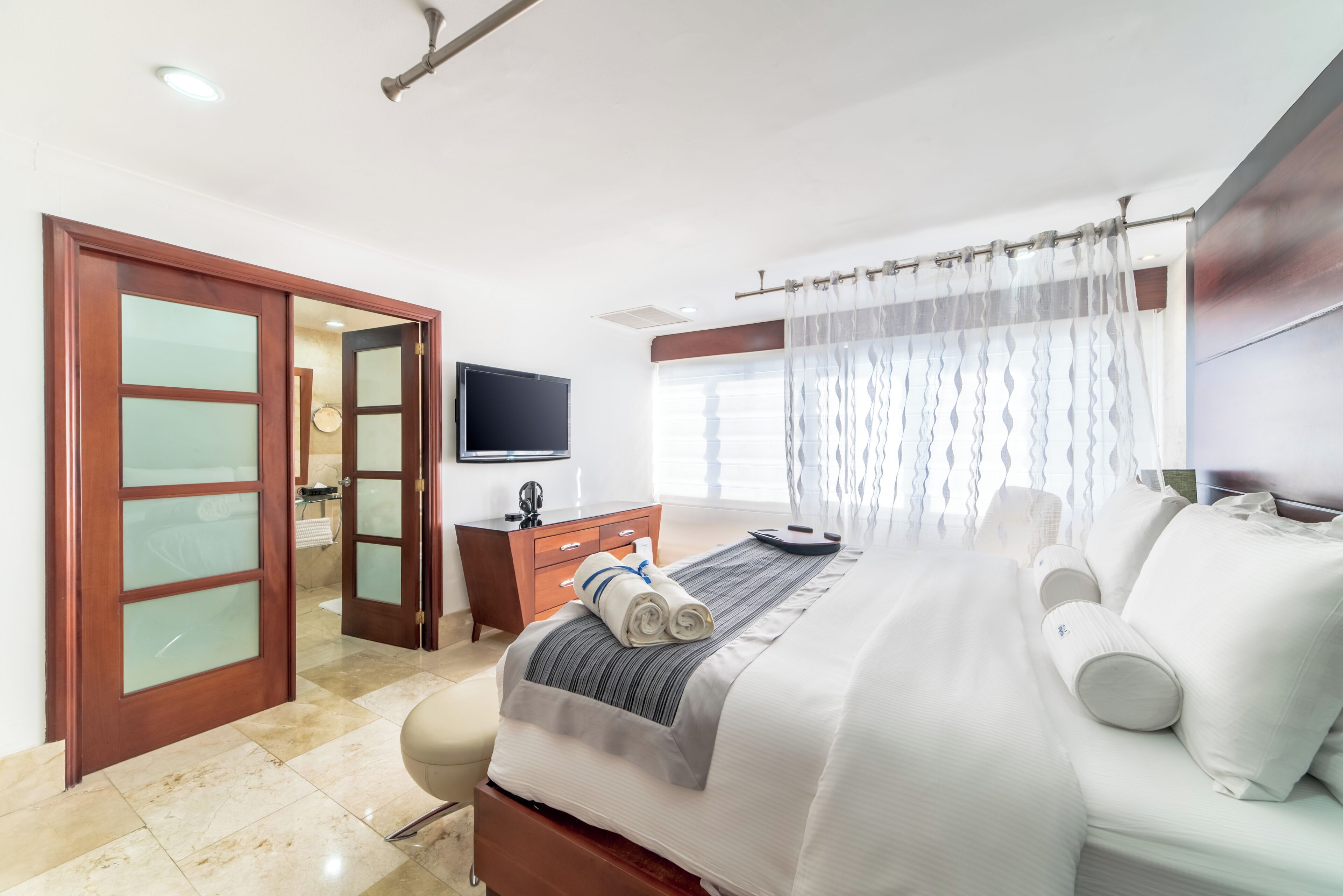 A hotel room with a bed, a TV, a desk, and a bathroom with a shower curtain.
