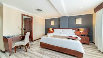 A hotel room with a wooden bed, a desk with a chair, a bedside table, and a nightstand.