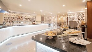 A modern hotel lobby with a reception desk, decorative white panels, and a buffet area with various food items. - Hodelpa Gran Almirante Hotel & Casino (Santiago de los Caballeros)