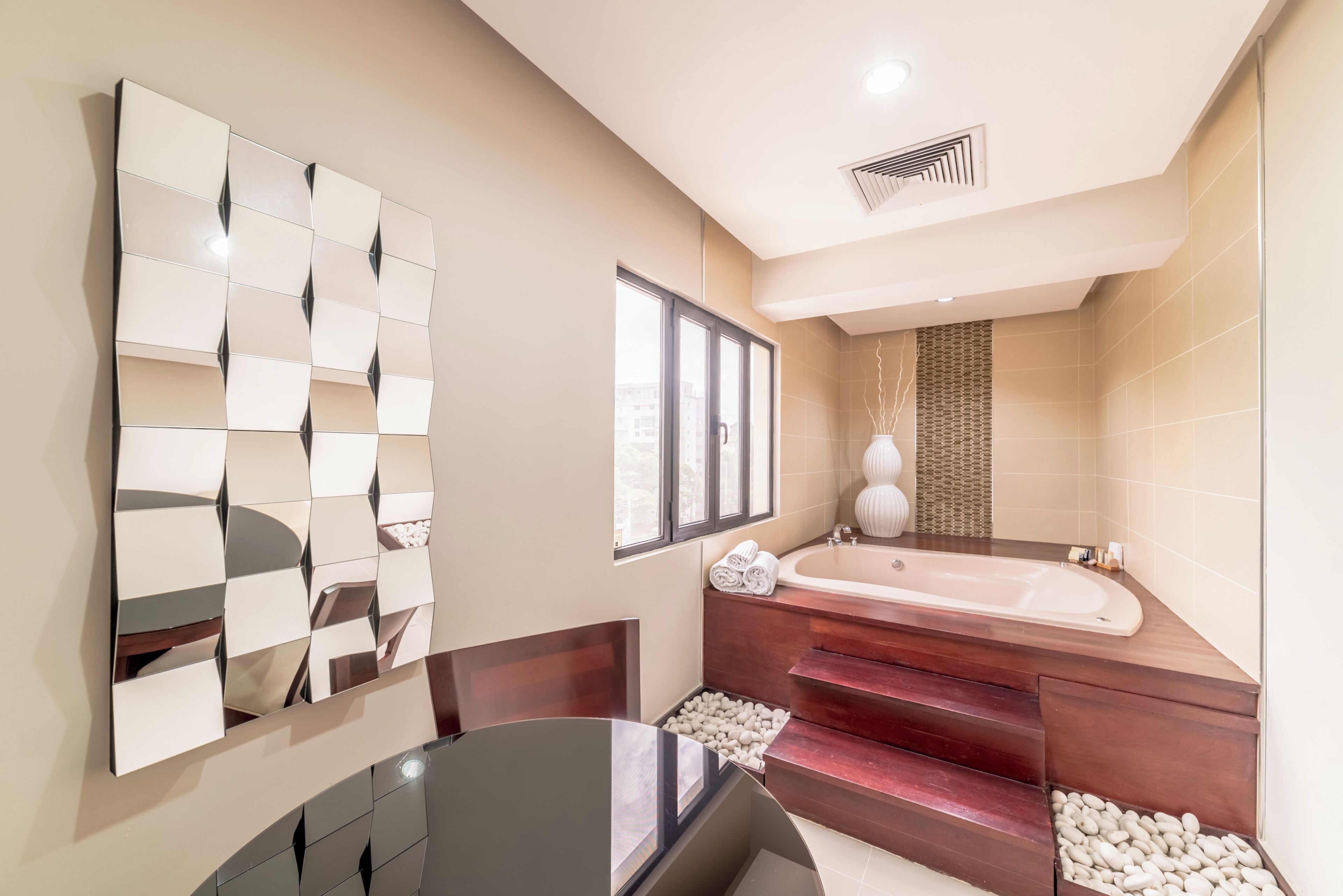 Un baño moderno con un espejo grande, una bañera y una zona de estar con una mesa.