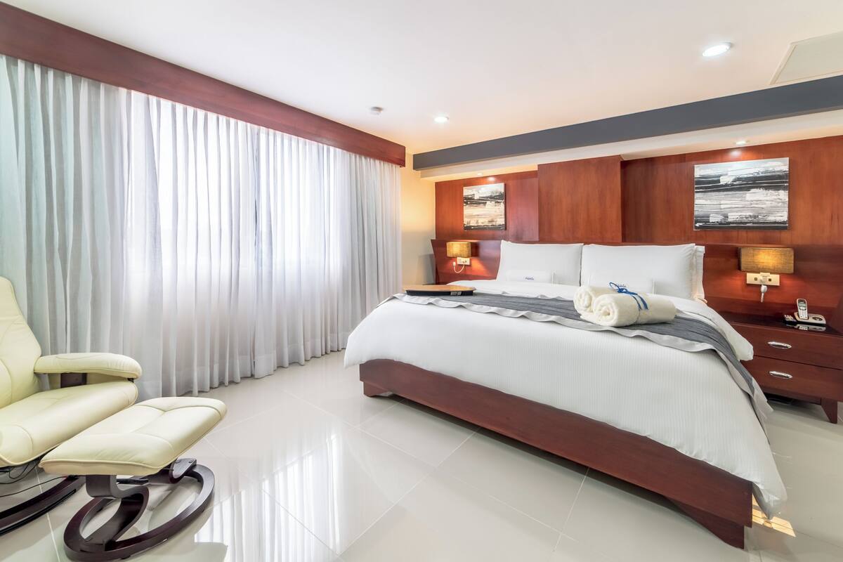 A hotel room with a large bed, a chair, a desk, and a telephone.