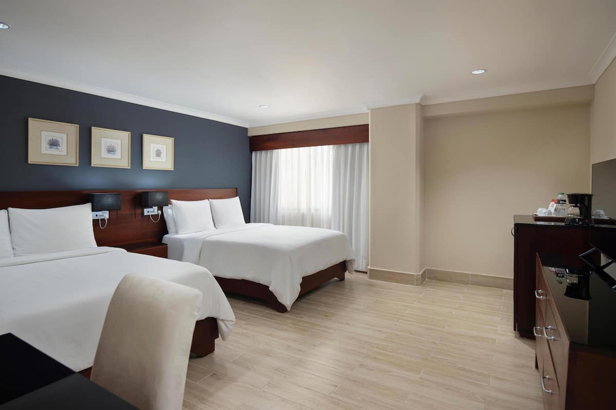 A hotel room with two beds, a desk, and a television.