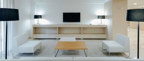 A modern, minimalist TV room with a flat-screen TV, two side tables with lamps, a wooden coffee table, and a sofa.