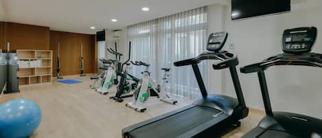 Un gimnasio con cintas de correr, bicicletas estáticas y una pelota de ejercicios azul.