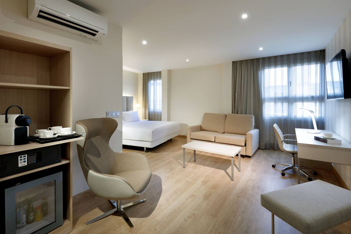 Ein modernes Hotelzimmer mit Bett, Sofa, Schreibtisch und einer Küchenzeile.