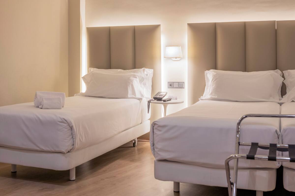 Ein Hotelzimmer mit zwei Betten, einem Nachttisch mit Lampe und einem Sessel.