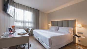 A hotel room with a bed, bedside table, desk, chair, TV, and window with curtains.
