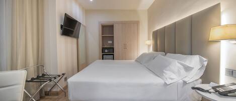 Une chambre d’hôtel comprenant un lit, un téléviseur fixé au mur, une table de chevet avec une lampe et un bureau avec un téléphone.