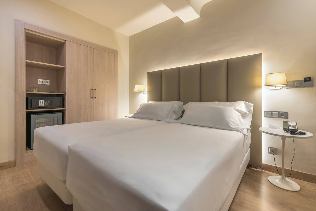 Ein Hotelzimmer mit einem großen Bett, einem Kleiderschrank, einem Nachttisch mit Lampe und einem kleinen Schreibtisch mit Telefon.