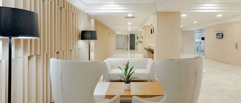 Un vestíbulo moderno con una recepción, dos sillones blancos, paneles de madera y un techo con iluminación empotrada.