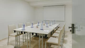 A conference room with a long table, chairs, a projector screen, and water bottles.