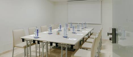 A conference room with a long table, chairs, a projector screen, and water bottles.