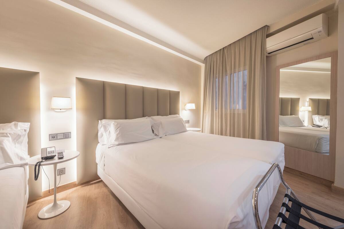 Ein Hotelzimmer mit einem großen Bett, Nachttischen, einem Spiegel und einer Klimaanlage.