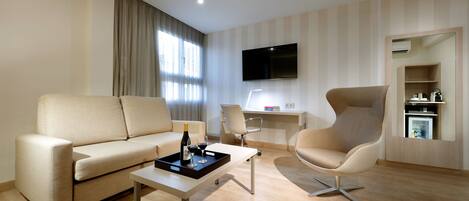 Una sala de estar moderna con un sofá, una mesa de centro con una bandeja de copas de vino y una botella, un escritorio con una silla, y un televisor montado en la pared.