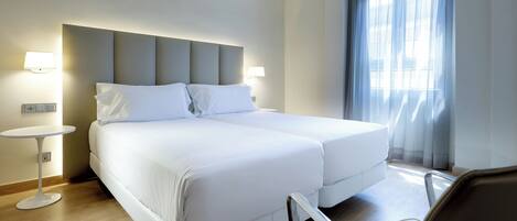 A hotel room with a double bed, two bedside tables, a chair, and a large window with curtains.