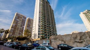 Un grand immeuble à étages, doté de balcons, entouré de voitures garées et de palmiers.