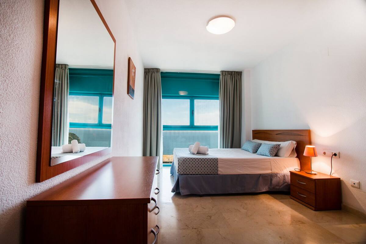 Un dormitorio con cama, mesita de noche, lámpara y un espejo grande.