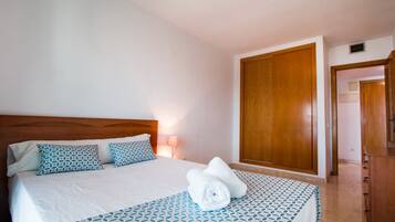 Una cama bien hecha con una colcha estampada, un cabecero de madera y un par de toallas enrolladas sobre la cama.