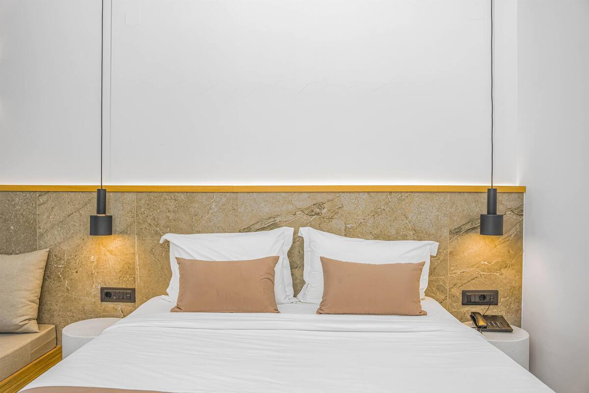 A hotel room with a bed, two bedside tables, a nightstand, a wall-mounted lamp, and a telephone.