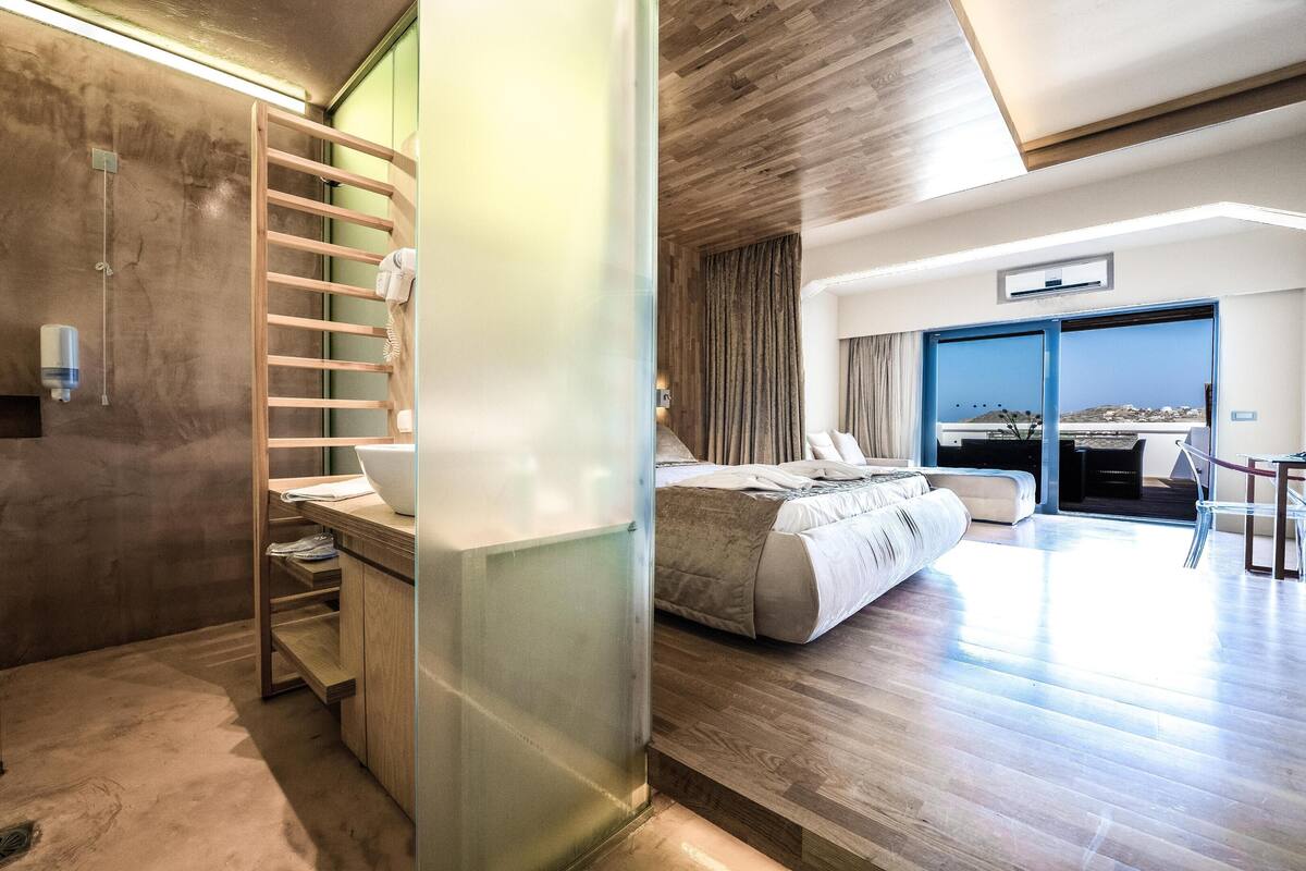 A modern hotel room with a large bed, a walk-in closet, and a balcony with a view.