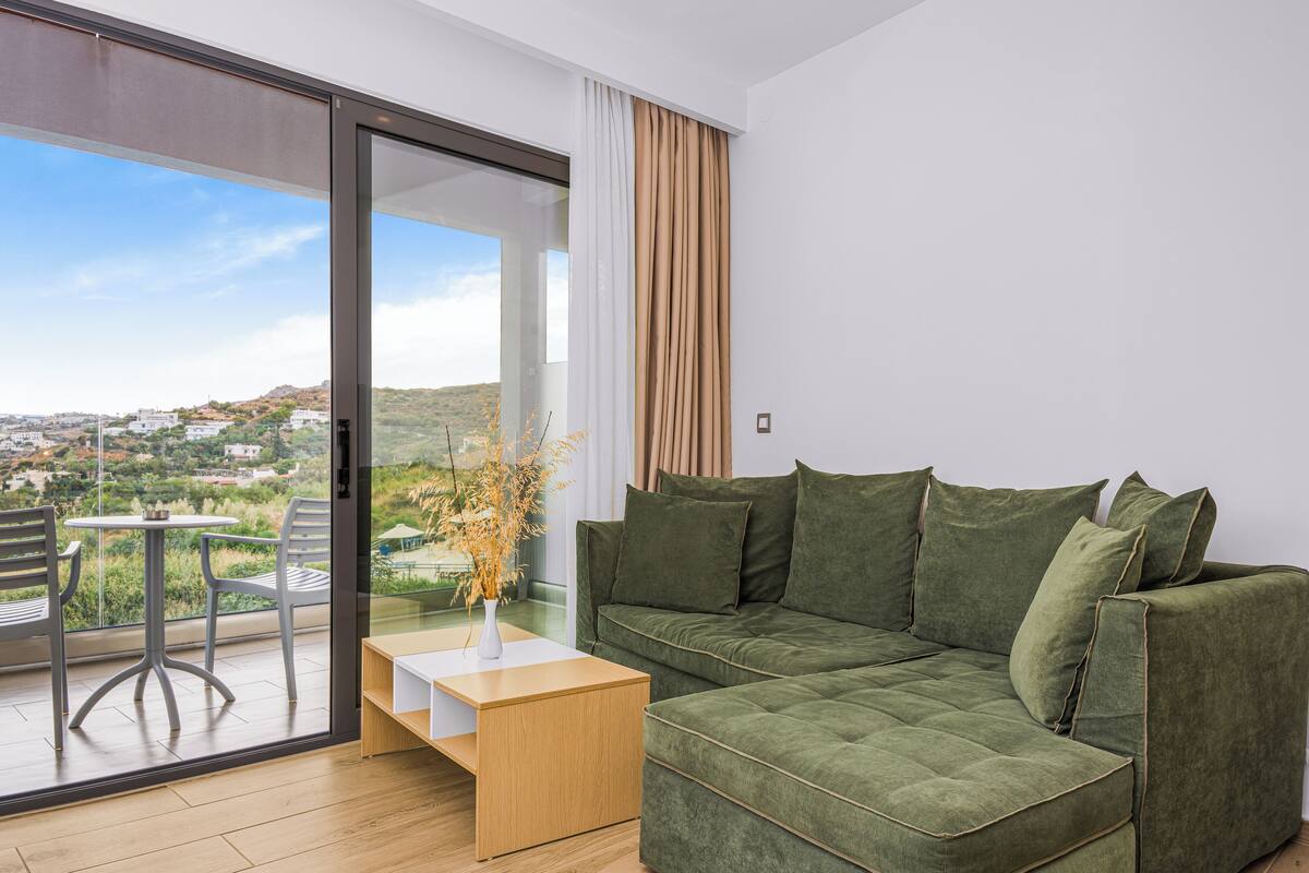 A modern living room with a green sofa, a wooden coffee table, and a view of a cityscape through a sliding glass door.