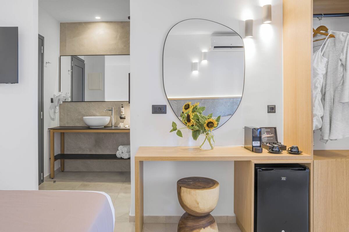 A modern bathroom with a wooden vanity, a sink, a mirror, a small refrigerator, and a vase with sunflowers.