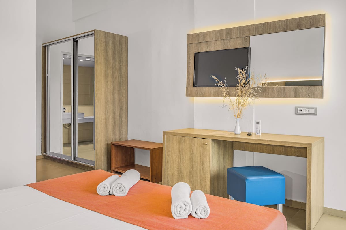 A hotel room with a bed, a wooden desk, a TV, and a sliding door.