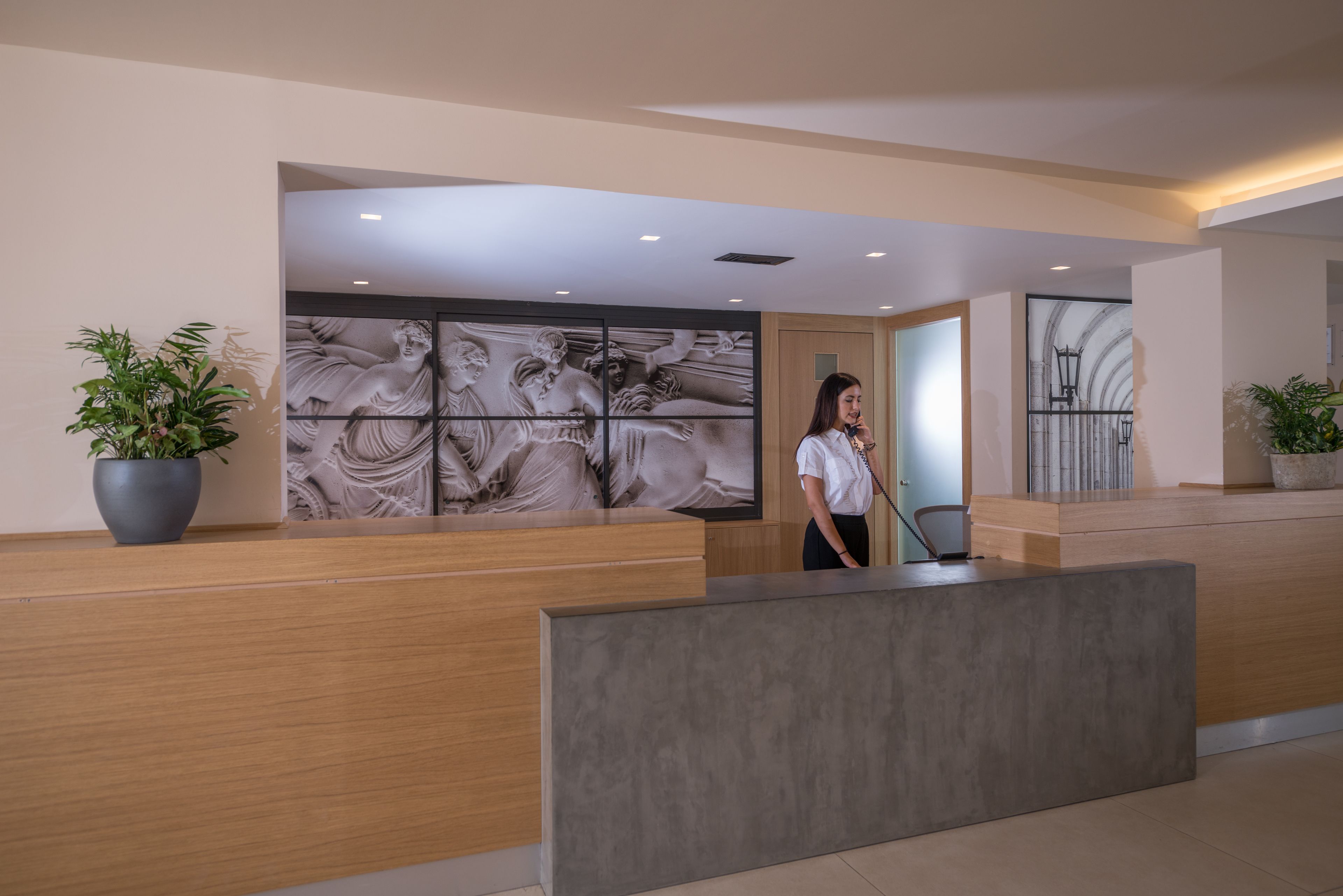 A reception area with a wooden reception desk, a large marble sculpture, and potted plants.