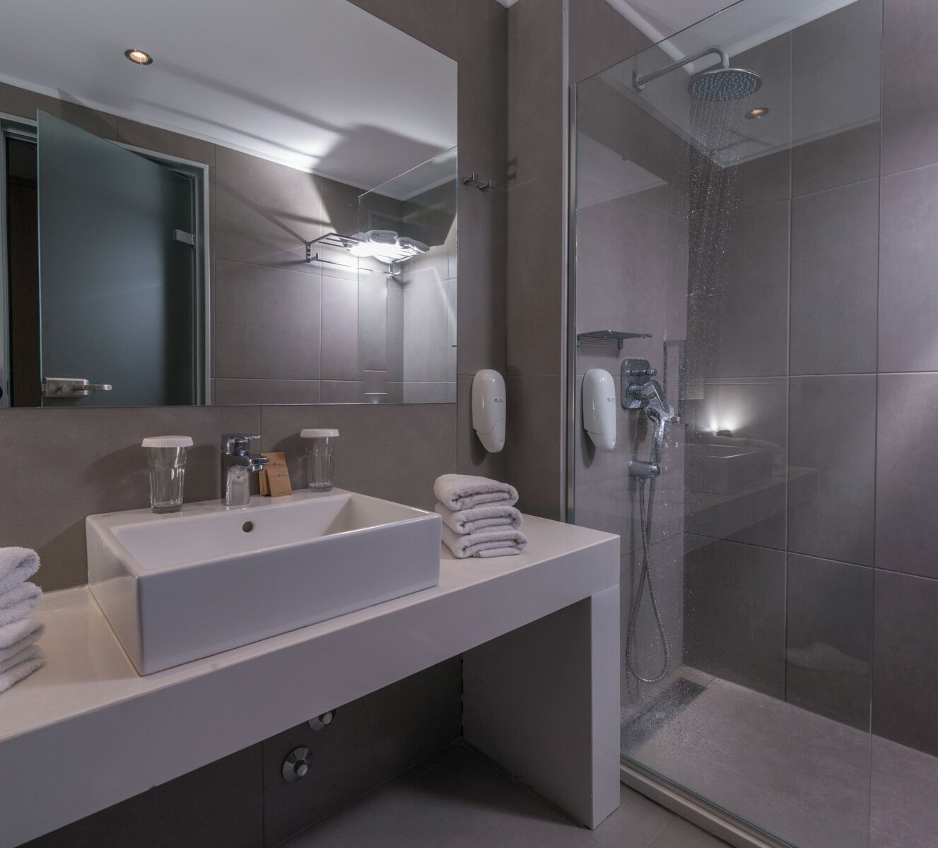 A modern bathroom with a large mirror, two sinks, a glass shower enclosure, and a towel rack.