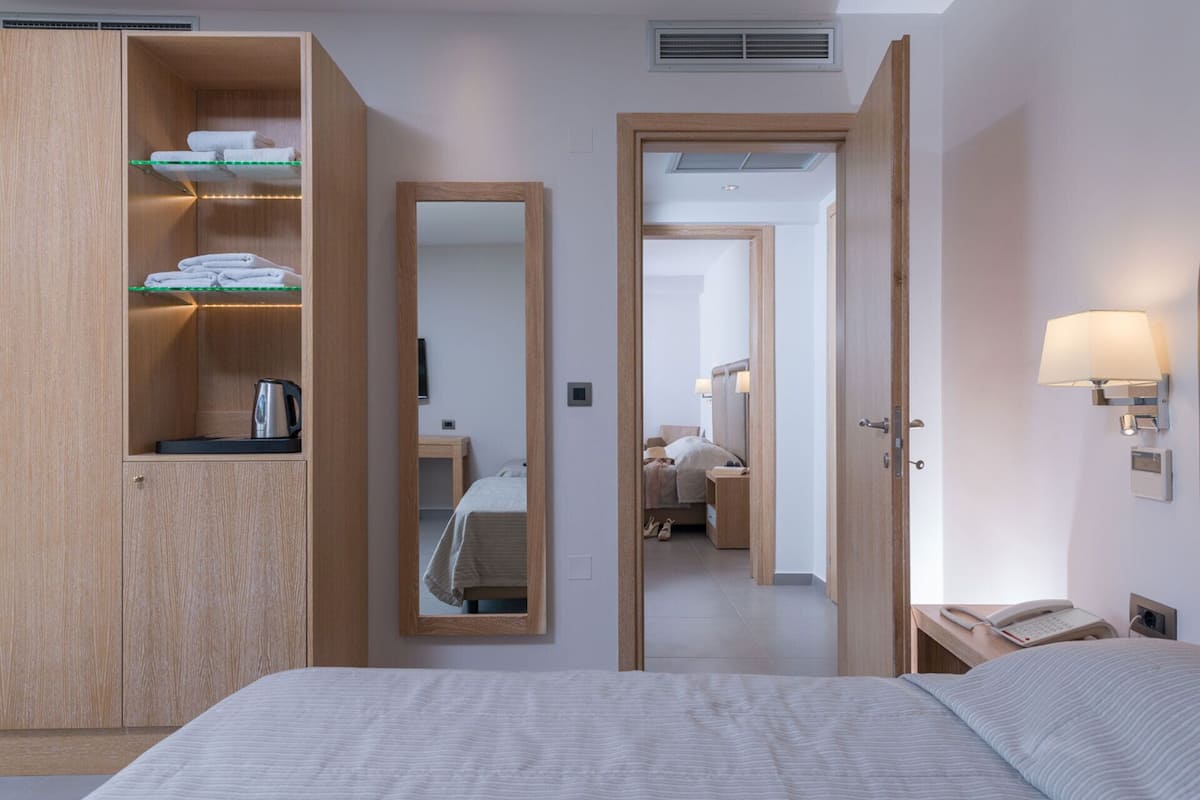Hotellihuone, jossa on sänky, puinen vaatekaappi hyllyineen, peili, yöpöytä lampun kanssa ja puhelin.