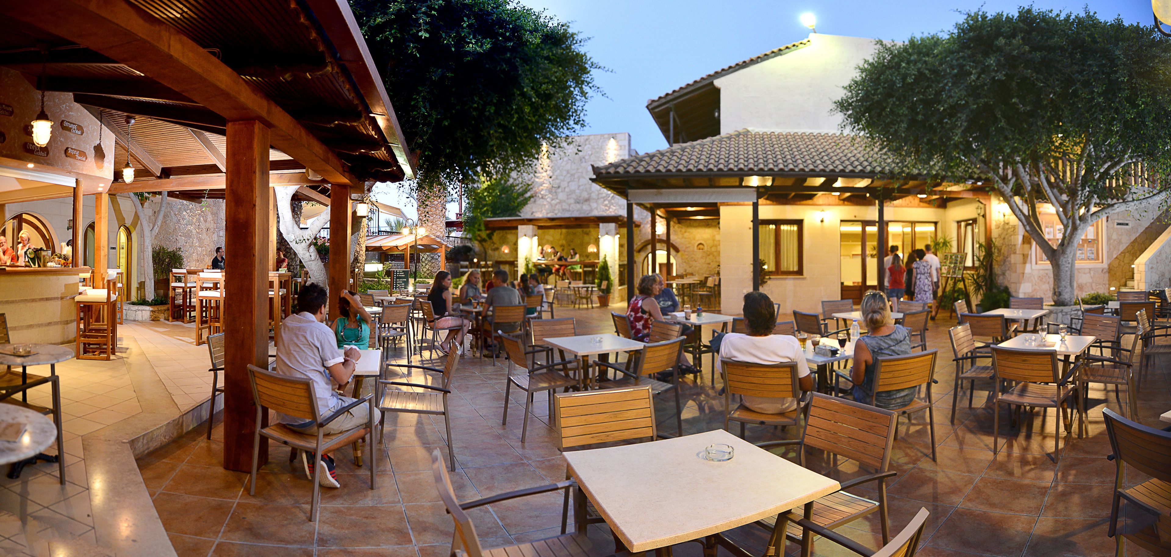 Un café al aire libre con mesas y sillas de madera, paredes de piedra y piso de baldosas.
