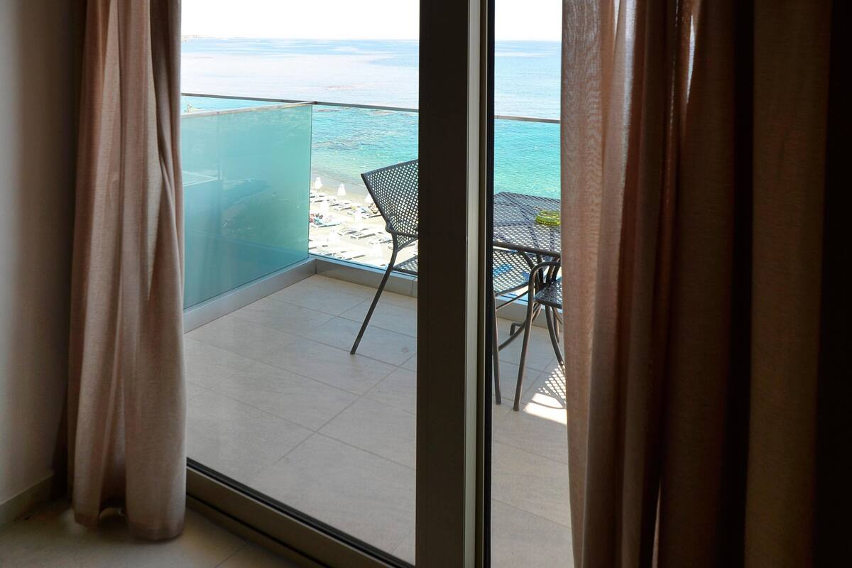 A balcony with a view of the sea, a table, and a chair.