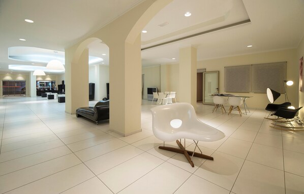 Un hall d’hôtel spacieux et moderne, au design minimaliste, comprenant un espace salon central, un comptoir d’accueil et un espace repas.