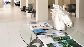 A spacious lobby with a glass table displaying magazines, a large horse sculpture, and modern seating areas. - Golden Beach Hotel (Hersonissos)