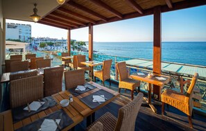 Un espace de restauration en plein air, avec des chaises et des tables en osier, offrant une vue sur une plage et la mer.