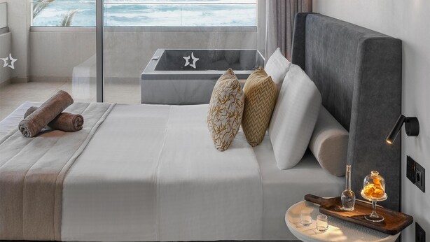 Un dormitorio moderno con una cama grande, una mesita de noche con bandeja y vistas al océano.
