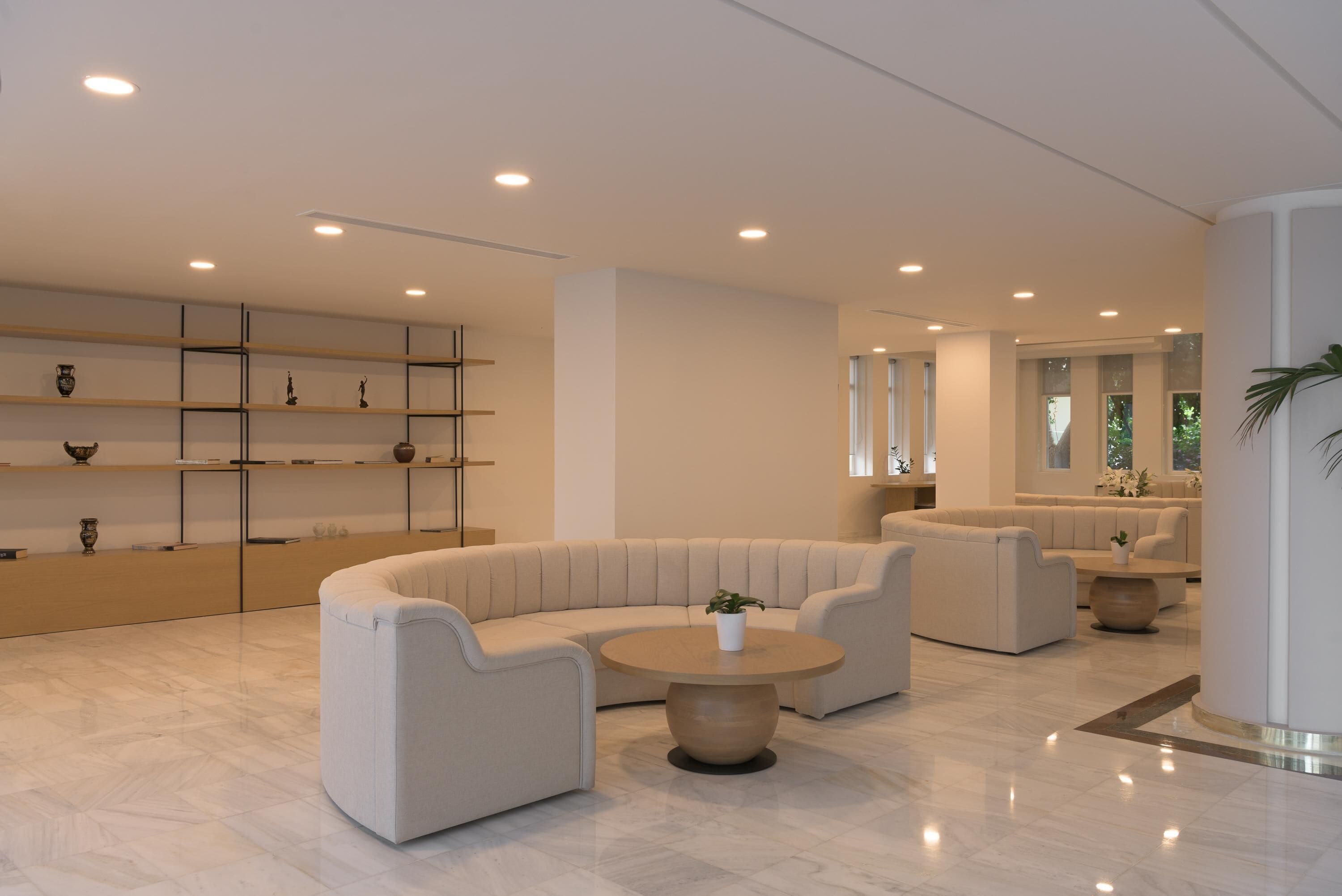 A modern, spacious lobby with a curved sofa, a round coffee table, and a minimalist shelving unit.
